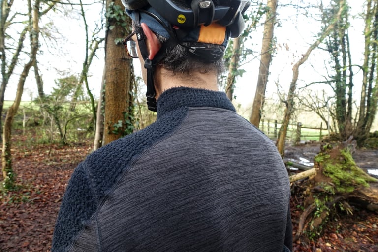 Rear view of the Velocio Alpha jersey, with a fleecy shoulder panel and a grey merino-backed back, worn under a helmet.