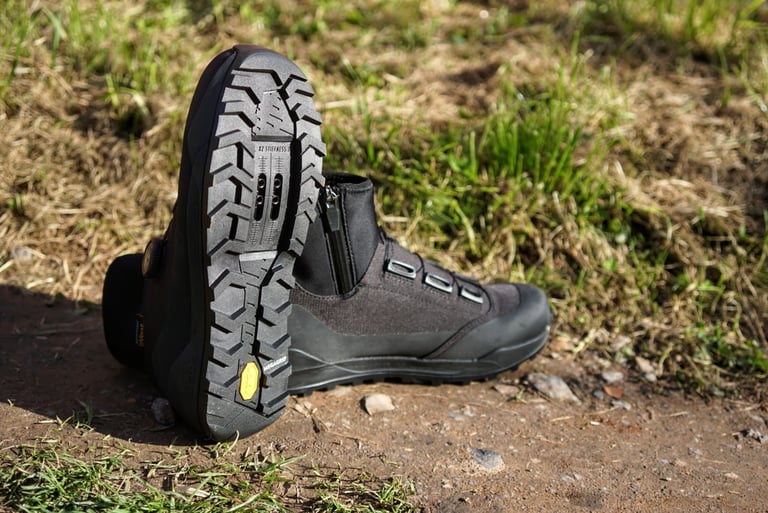 Sole of a Fizik Terra Artica X2 boot with Vibram Megagrip chevron tread and cleat slots, beside its pair.