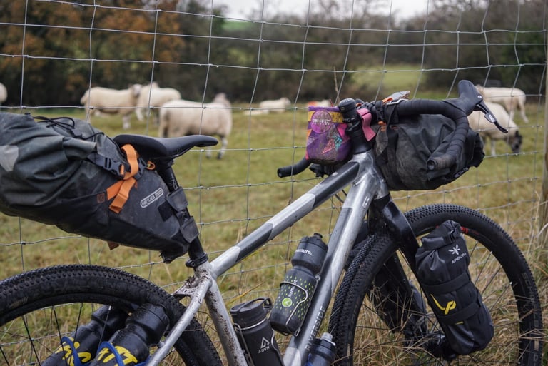 Ortlieb seat post pack sitting snug against the saddle and seat post of a bike leaning on a fence by a sheep field.
