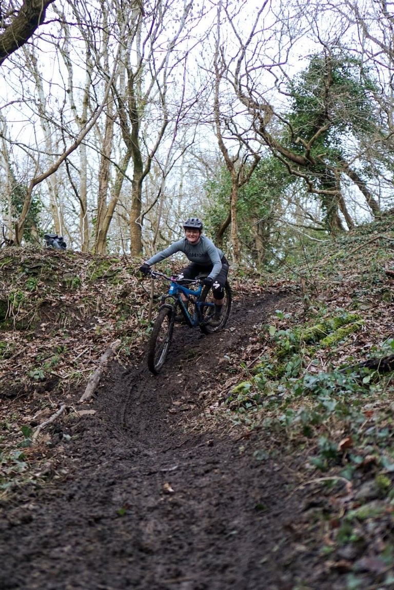Mountain biker in a grey Cascada merino baselayer rides a muddy woodland descent on a blue bike.