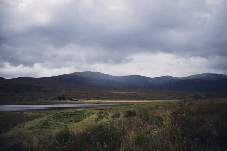 Low grey cloud over the hills above Loch Luichart, with a lone cottage on the moor beyond the water.