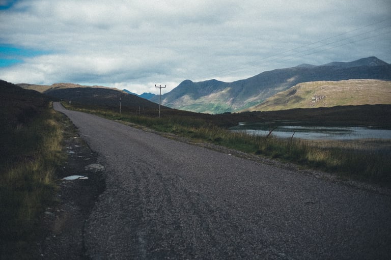 Empty narrow road running past a loch towards cloud-topped mountains on the tandem route through the Highlands.