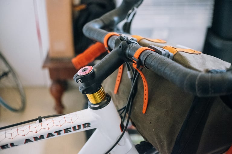 Handlebar and stem of a white gravel bike with a canvas bag strapped to the bars, set up before building the support.