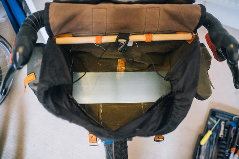 Inside the open canvas handlebar bag, an aluminium plate sits in the base to test its position.