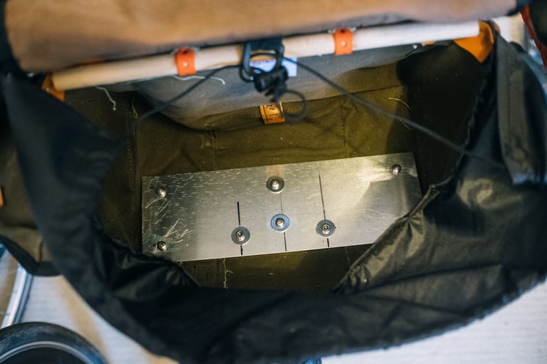 Aluminium plate bolted into the base of the canvas bag with washers and nuts, seen from above.
