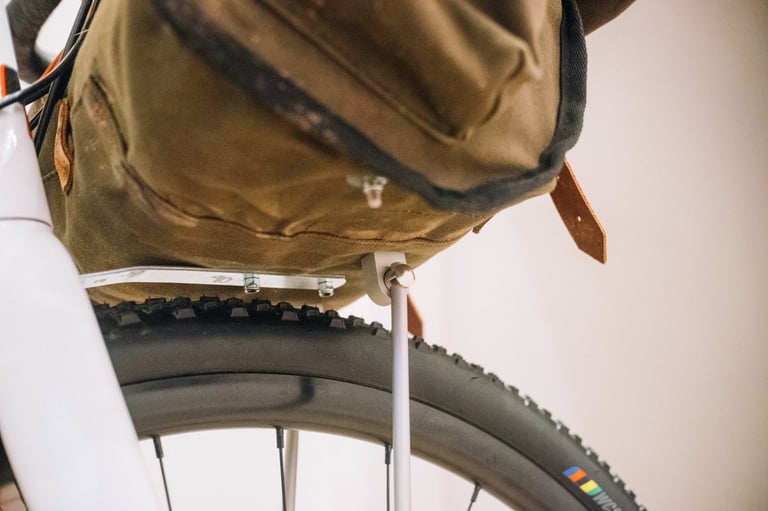 Underside of a canvas handlebar bag resting on the finished aluminium plate and strut support above the front tyre.