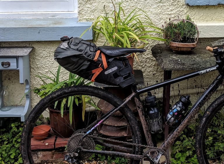Large Ortlieb seat post pack fitted to a muddy bike propped against a garden wall.