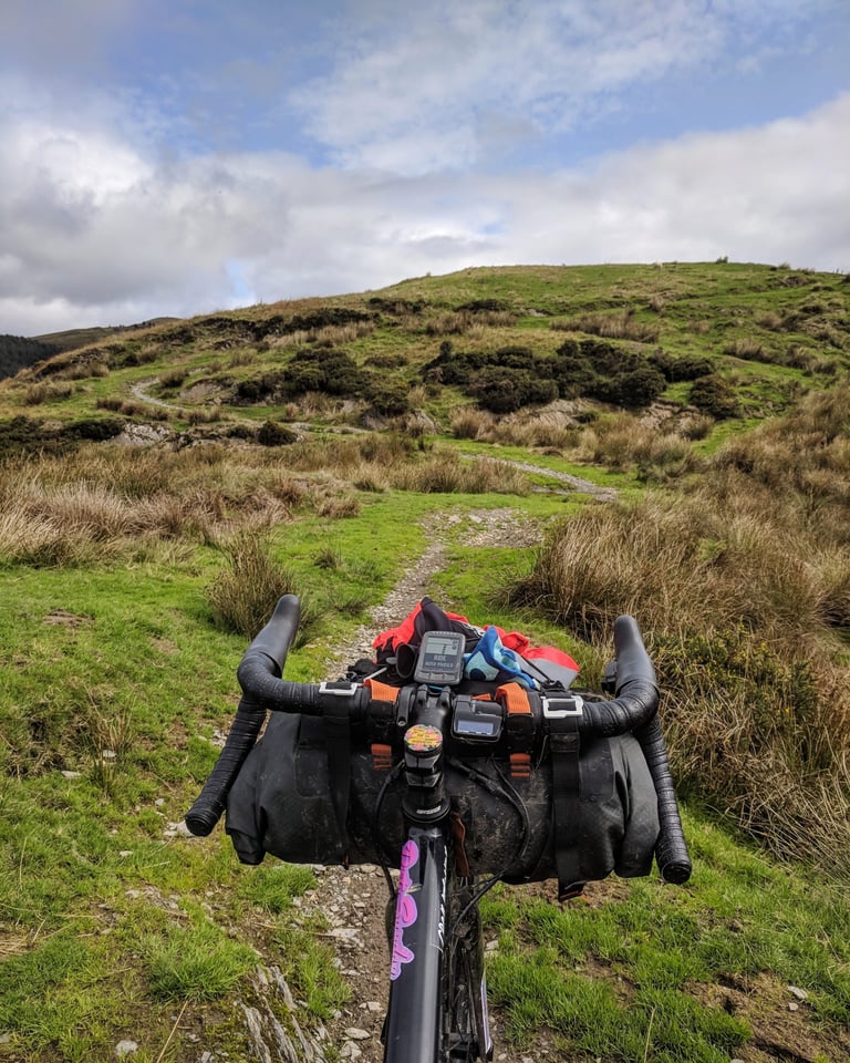 Ortlieb handlebar pack stretched between drop bars with a bike computer, on a grassy hill track.
