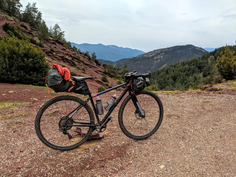 Bikepacking bike with an Ortlieb seat post pack and a jacket tucked under its bungee cords, on a red hillside track.