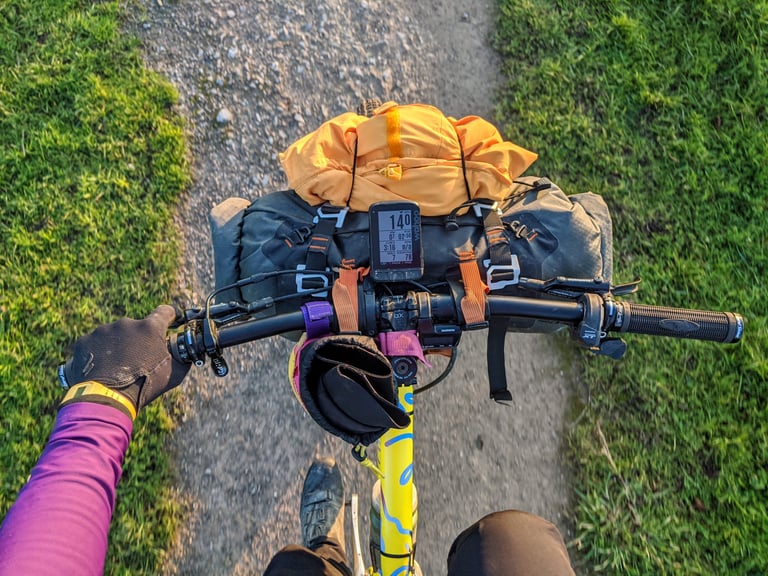 Looking down on an Ortlieb handlebar pack with a jacket strapped on top, mounted on flat bars on a gravel path.