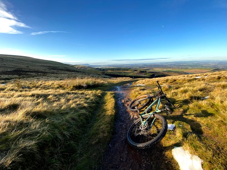 Mint Cale AL lies on its side on a muddy Pentland Hills track, rear wheel nearest the camera and farmland far below.