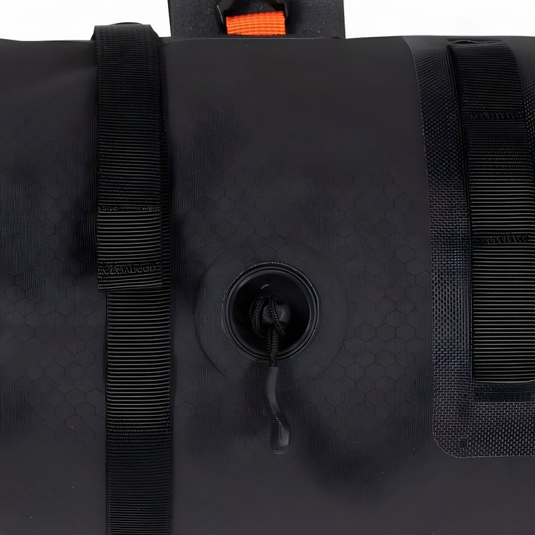 Close-up of the one-way air valve on the back of a black Ortlieb handlebar pack, between two webbing straps.