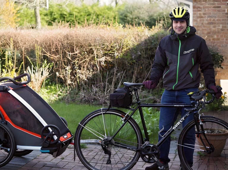 Fasted 500 founder Zahir Nayani in a helmet and jacket standing beside his bike and child trailer.