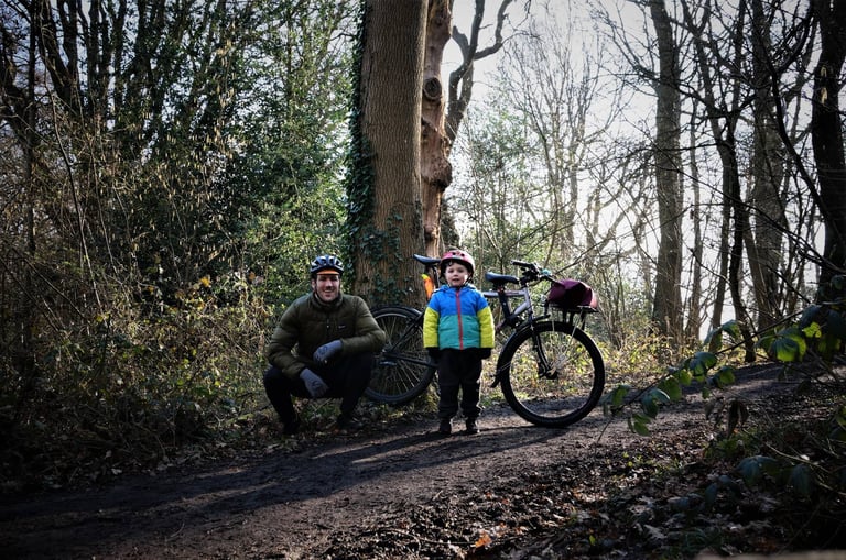 Adult and child in helmets beside a bike on a woodland track, on a pirate-themed treasure-hunt ride around Croydon, London.