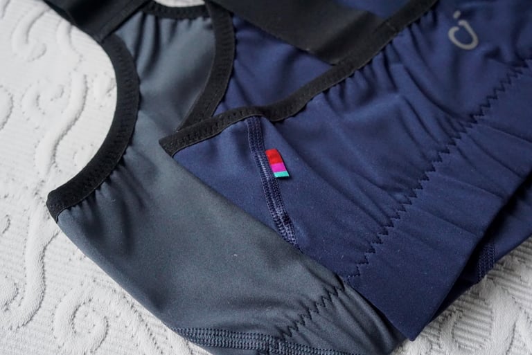 Velocio LUXE bra in navy laid flat, close-up of the small multicoloured tag on the seam at the back.