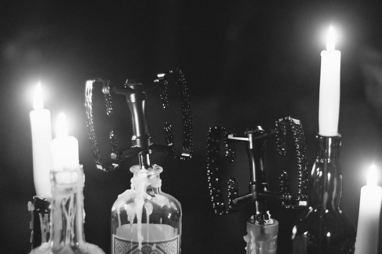 Two black SimWorks Bubbly pedals mounted on glass bottles among lit candles, in a moody black-and-white shot.