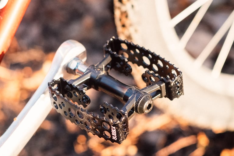Close-up of a black SimWorks Bubbly pedal on a silver crank, showing the toothed, hole-pierced metal cage.