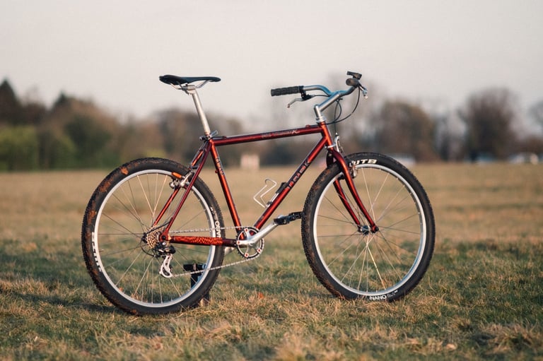 Red Trek mountain bike fitted with SimWorks Bubbly pedals, standing on grass with trees behind.