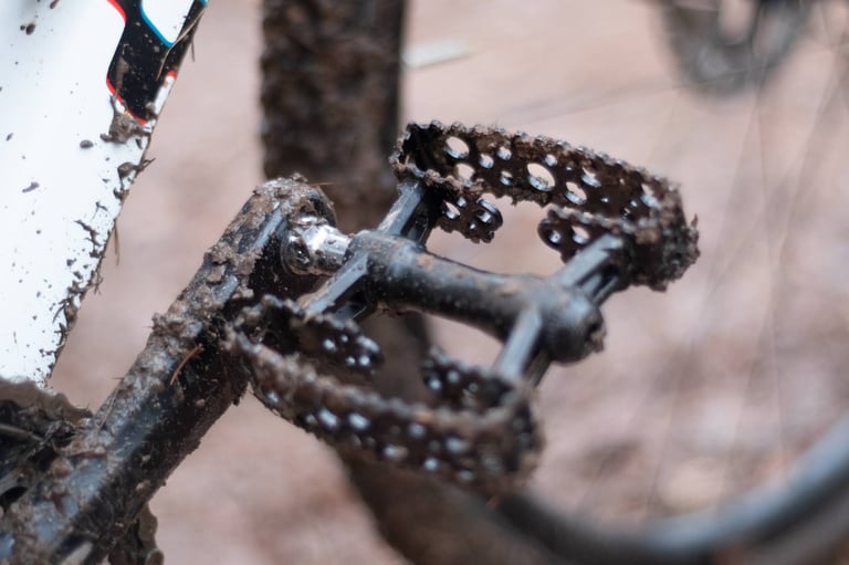 Mud-caked SimWorks Bubbly pedal and crank after a wet ride, with a muddy tyre behind.
