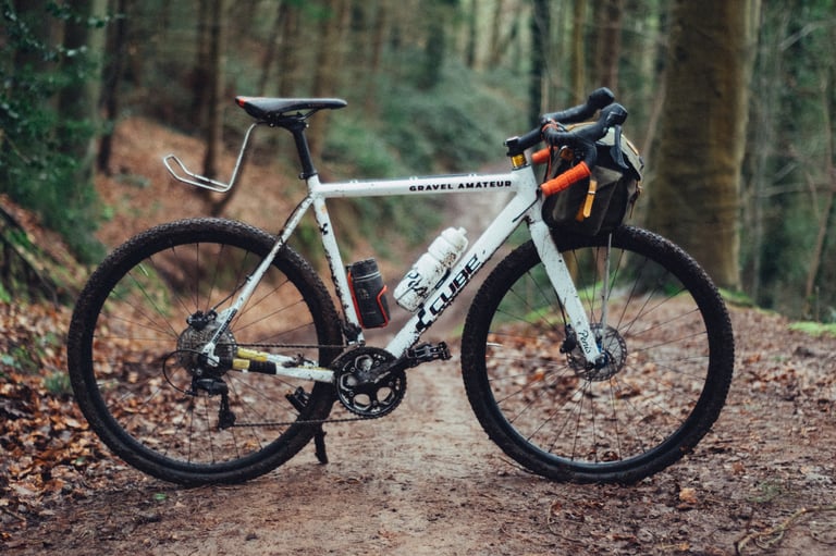 Muddy white Cube bike fitted with SimWorks Bubbly flat pedals, with a bar bag, on a leafy woodland track.