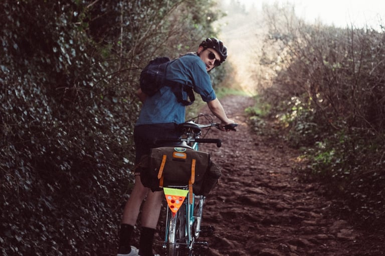 Cyclist in a blue shirt looks back on a muddy lane wearing the smaller Chrome Mini Kadet, with a bag on the rear rack.