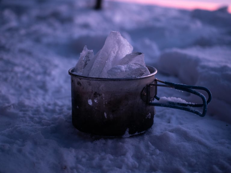 Battered camping pot filled with chunks of ice on the snow at dusk, melted for drinking water on the Baikal trip.