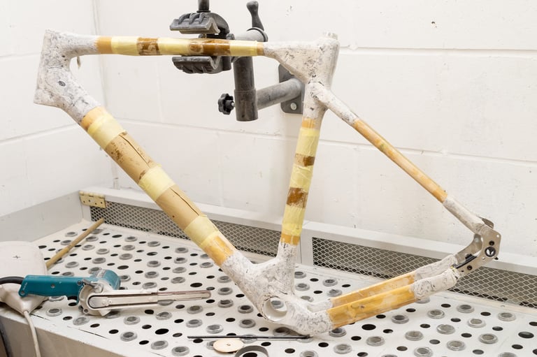 Bamboo bicycle frame with flax composite joints held in a workshop stand beside a belt sander.
