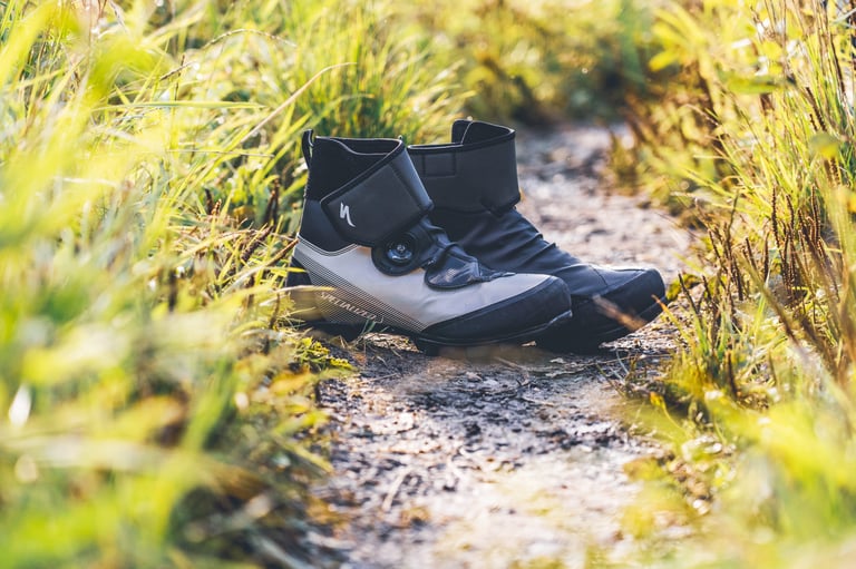 Pair of Specialized Defroster winter boots on a narrow muddy trail between long grass.