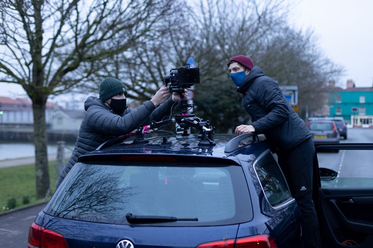Two crew members in face masks rig a camera on a suction mount on a car roof while filming The Tipping Point.
