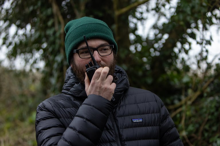 Co-director Jamie Edwards, in a green beanie, talks into a handheld radio on location for The Tipping Point shoot.