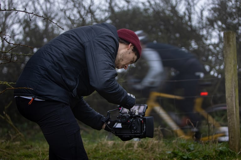 Cinematographer Dom John films a blurred rider on a yellow bike through a wire fence on The Tipping Point shoot.