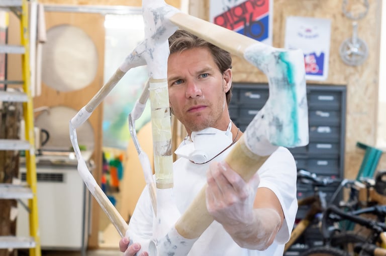 Maker in a dust mask holds up a bamboo gravel bike frame joined with flax fibre composite at Bamboo Bicycle Club.