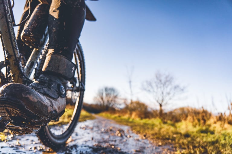 Mud-splashed Specialized Defroster boot on a pedal, seen from low down on a puddled winter track.