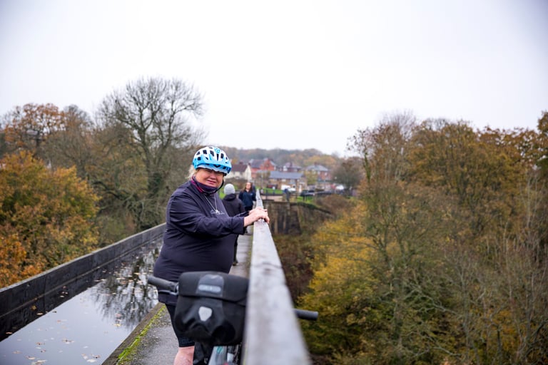 Smiling bikepacker in a blue helmet pauses on a canal aqueduct in North Wales, handlebar bag in the foreground.