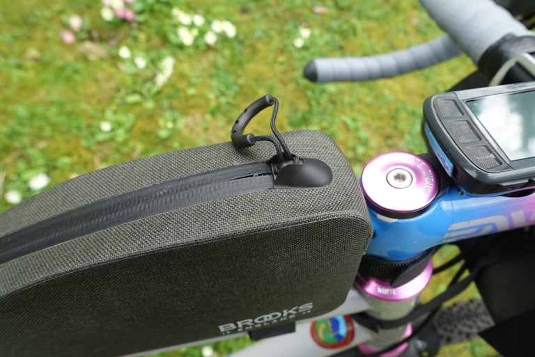 Top of the Brooks Scape top tube bag with its waterproof zip and looped pull cord, beside a pink and blue stem.