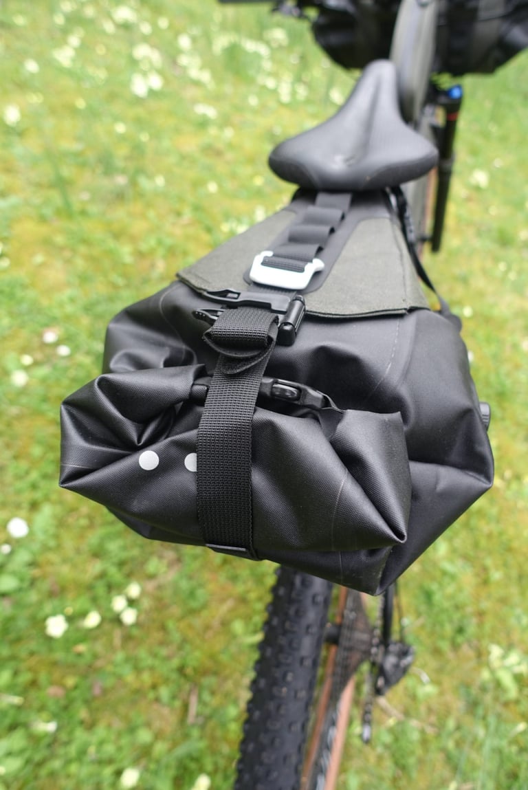 Rear view of the Brooks Scape Seat Bag on a bike, its black roll-top dry bag cinched with a webbing strap and buckle.