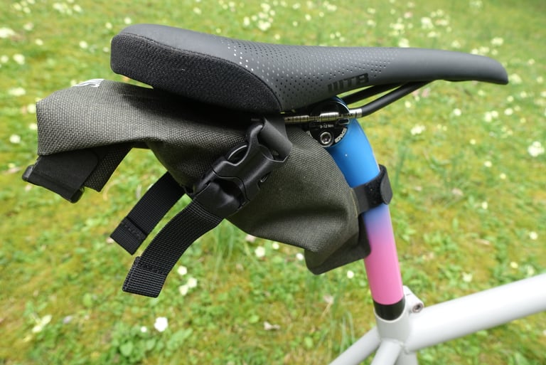 Brooks Scape Saddle Roll Bag hanging under a saddle and strapped to a blue and pink seat post with a Velcro strap.