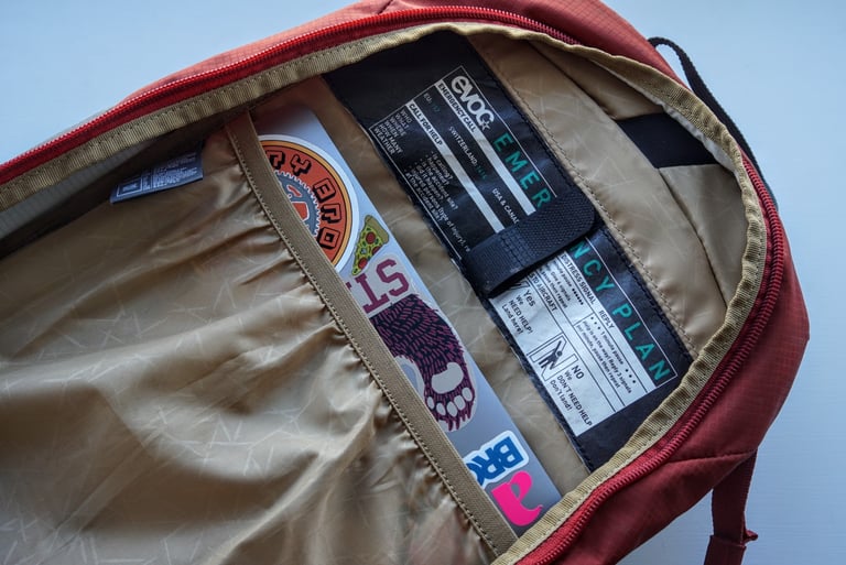 Laptop in the back sleeve of the EVOC Ride 12L, beside the printed emergency plan label.