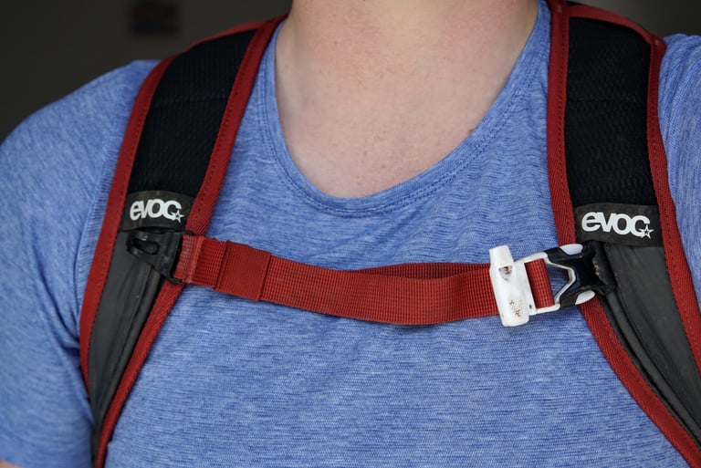 Red chest strap with a white emergency whistle buckle on the EVOC Ride 12L shoulder straps.