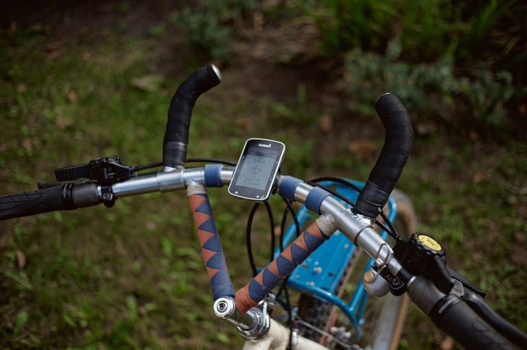 Converted vintage MTB handlebar with bar ends, a Garmin computer and a blue front rack ahead of the bars.