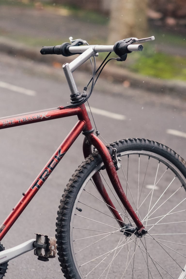 Long quill stem and flat bar on a red vintage Trek Mt. Track mountain bike parked on a wet road.