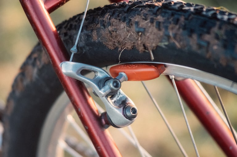Cantilever rim brake with a Kool-Stop Salmon pad on a red steel fork, beside a muddy knobbly tyre.