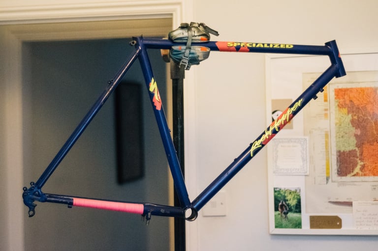 Bare navy Specialized Rockhopper frame with neon decals on a workshop stand, a bargain vintage MTB ready to build.