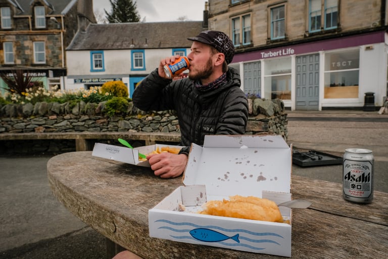 Rider drinks Irn-Bru beside a box of fish and chips at a picnic table in Tarbert, Argyll.