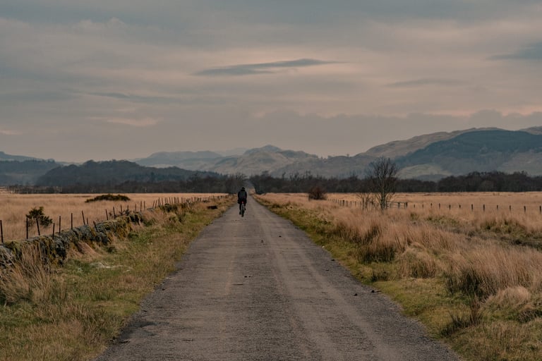 Lone rider on a quiet road across open grassland towards hills on the way up to Loch Awe.