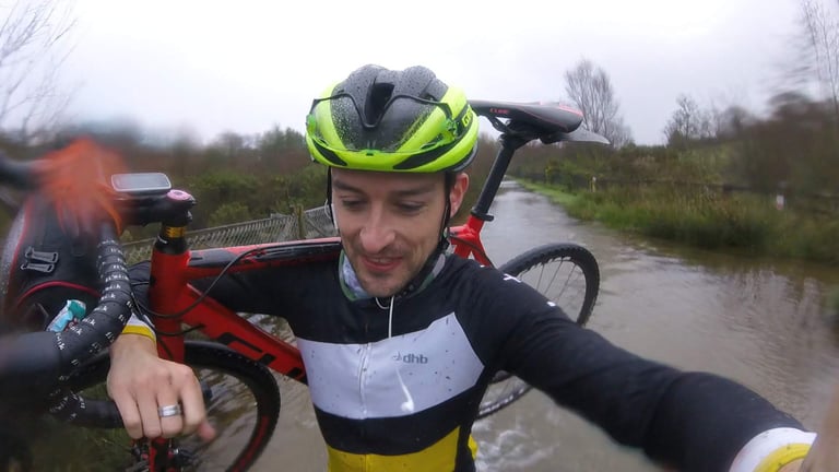 Rain-soaked selfie of a rider in a yellow helmet shouldering the red Cube Cross Race Pro through a flooded path.