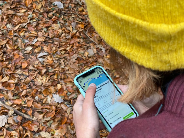Rider in a yellow beanie checks a planned cycling route on a phone navigation app, autumn leaves underfoot.