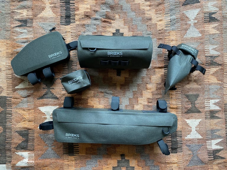 Brooks Scape top tube bag, handlebar pouch, frame bag, saddle pocket and saddle roll bag laid out in deep green.