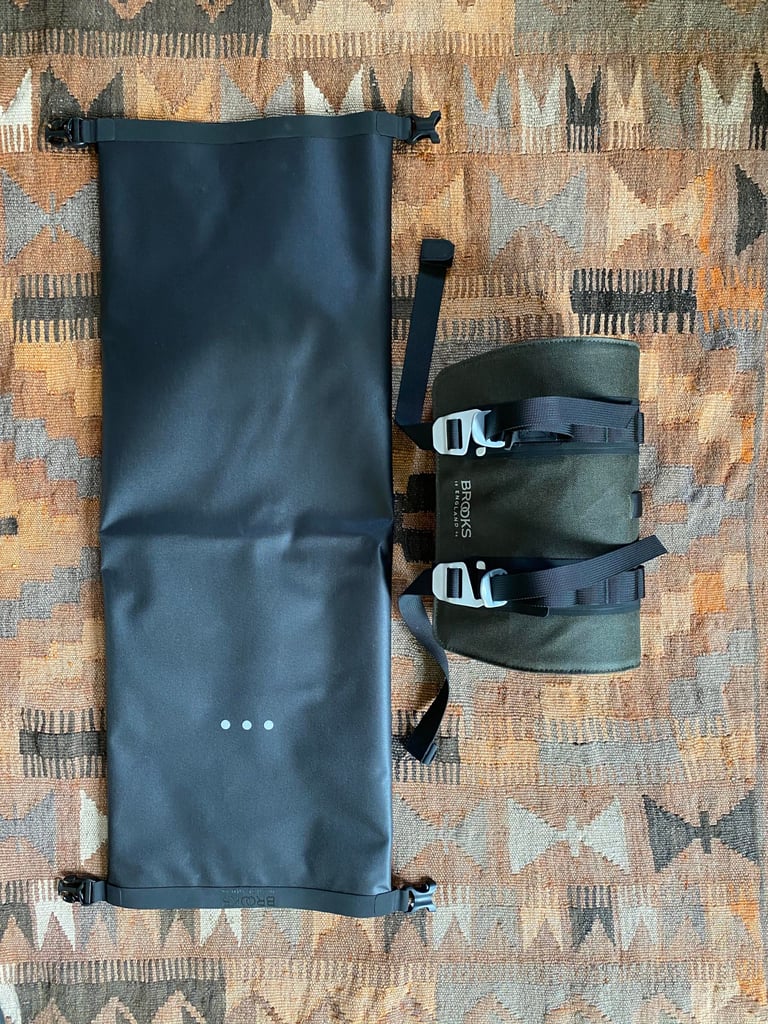 Brooks Scape Handlebar Roll split into its long black dry bag and the green holster, laid flat on a patterned rug.