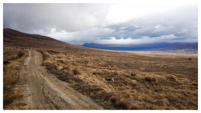 Rough track crossing open moorland on the Road To The Isles, with distant hills and heavy cloud, Central Highlander route.